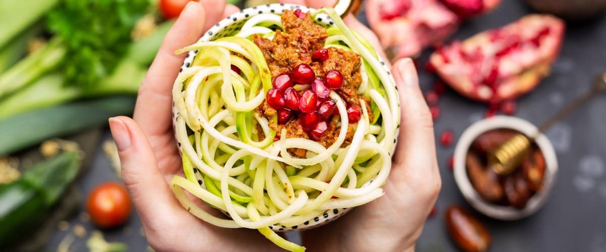 Top view of a vegan meal with spiralized zucchini, tomato sauce and pomegranates in the cup